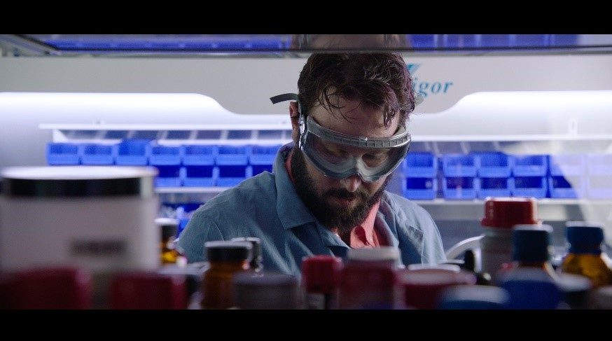 A scientist in safety goggles examines lab materials in a well-organized laboratory.