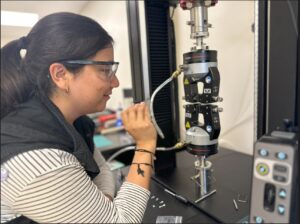 A student wearing goggles, watching as her sample goes into a Instron mechanical tester